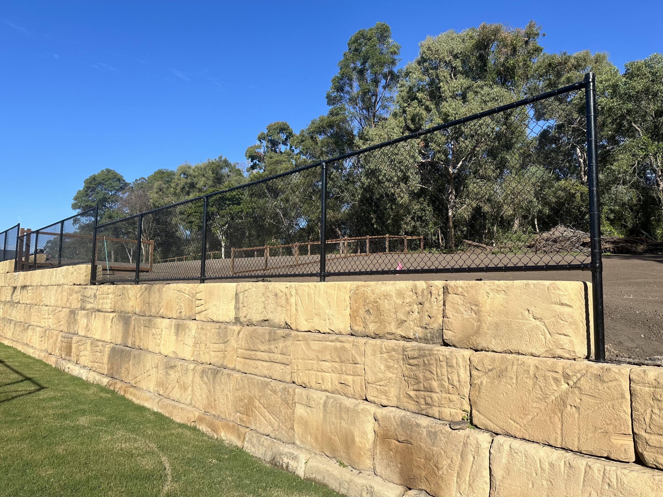 1200mm high black chainwire fence with posts grouted into core drilled Sandstone Block Wall - Wood Trades x QFence